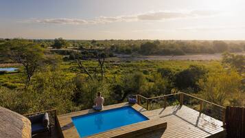 A wooden deck with a pool, overlooking a savanna landscape.