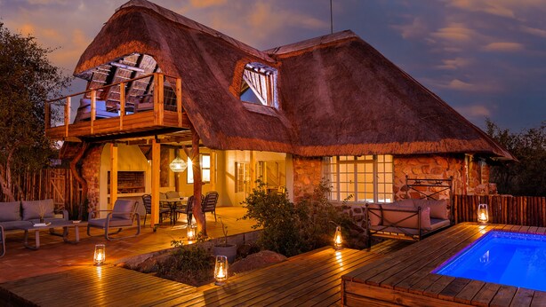 A thatched-roof house with a pool, outdoor seating, and a stone wall. - Simbavati Mvubu (Bushbuckridge)