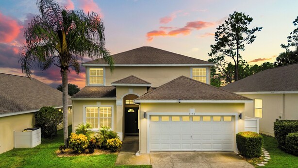 A two-story house with a garage, a front entrance, and a well-maintained lawn with bushes and a palm tree. - This charming 5-bedroom villa with a private heated pool is a modern oasis. (Davenport)