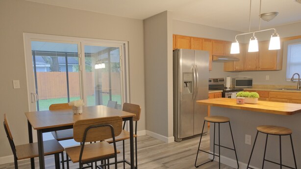 A modern kitchen with a stainless steel refrigerator, wooden cabinets, and a bar stool area. - Awalk away from Busch Gardens and Adventure Island (Tampa)