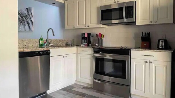 A modern kitchen with white cabinets, stainless steel appliances, and a granite countertop. - End unit townhouse (Baton Rouge)