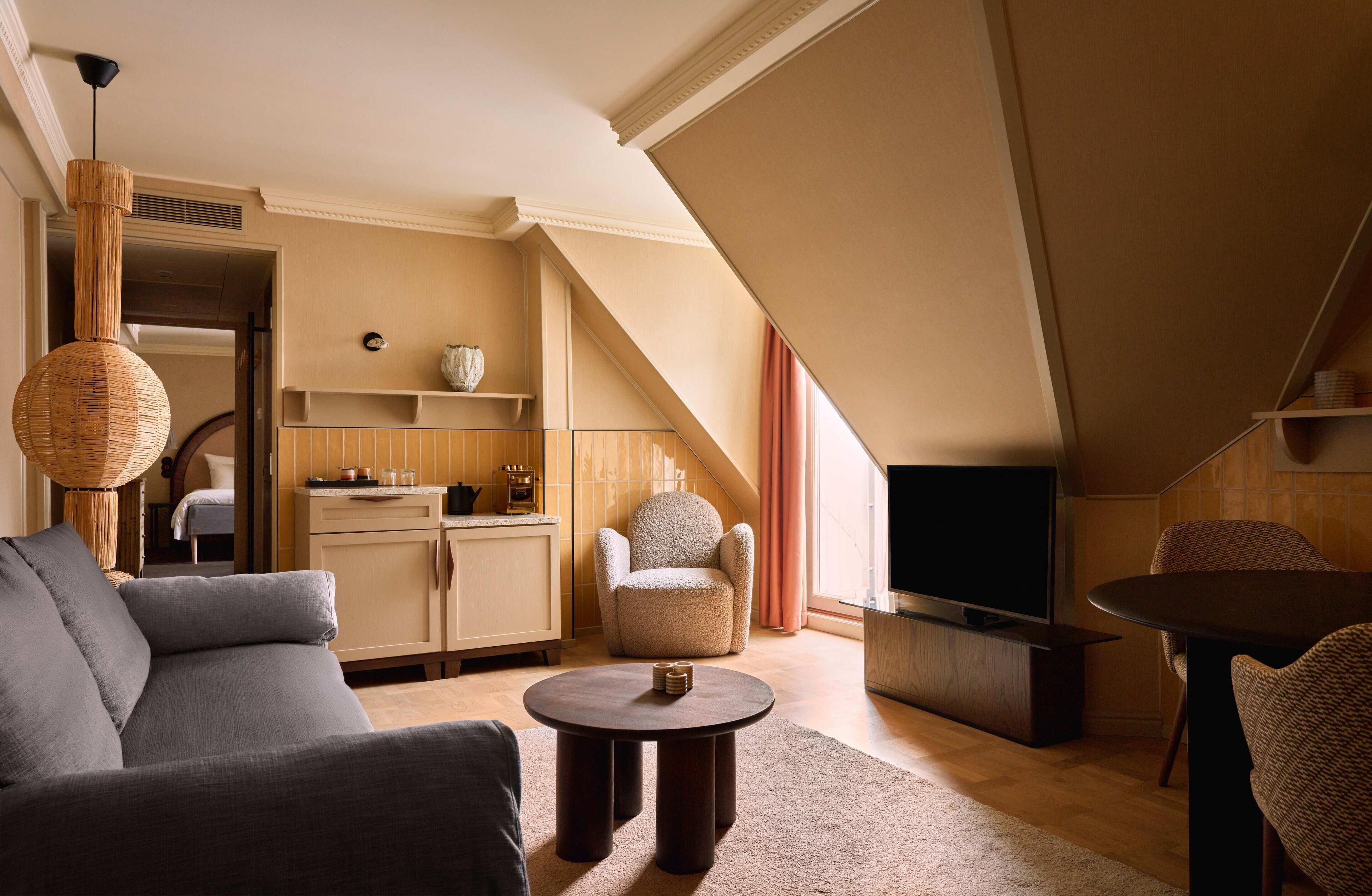 Una sala moderna con sofá, sillón y mesa de centro, televisor, y una zona de cocina con mesa y sillas de comedor.