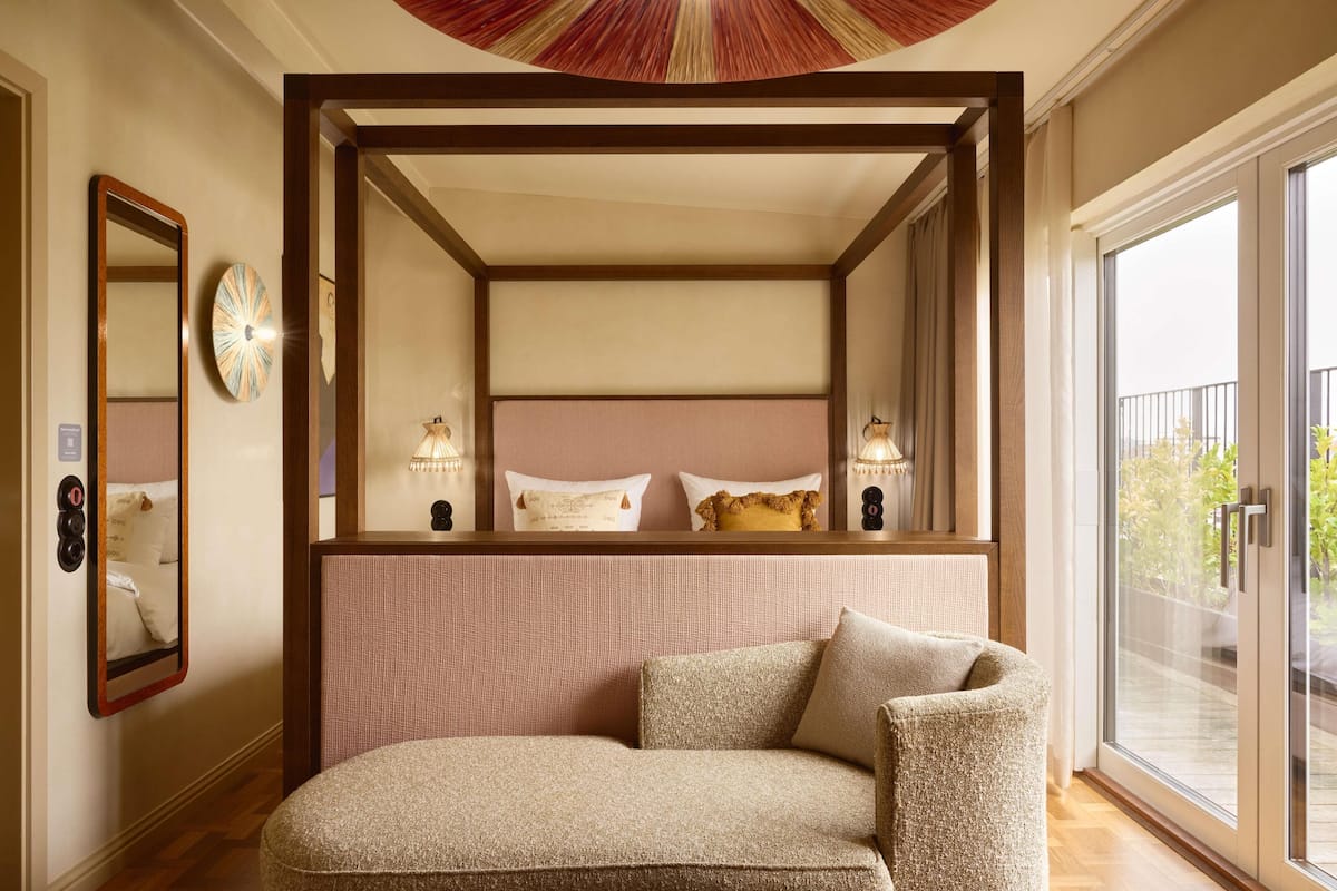 A bedroom with a four-poster bed, a large mirror, bedside lamps, and a view of the outdoors through a sliding glass door.