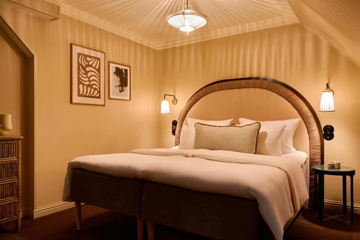 A hotel room with a large bed, a bedside table, and two wall-mounted lamps.