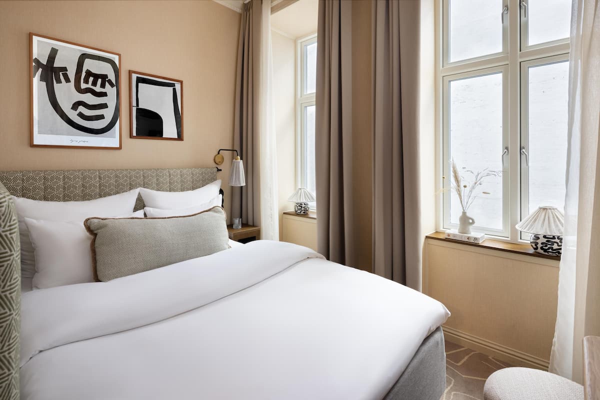 A neatly made bed with white linens, a headboard with a geometric pattern, and two wall-mounted artworks.