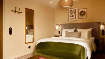 Habitación de hotel con una cama grande, un sofá verde, una mesa de madera, un espejo, luces fijadas en la pared y obras de arte.