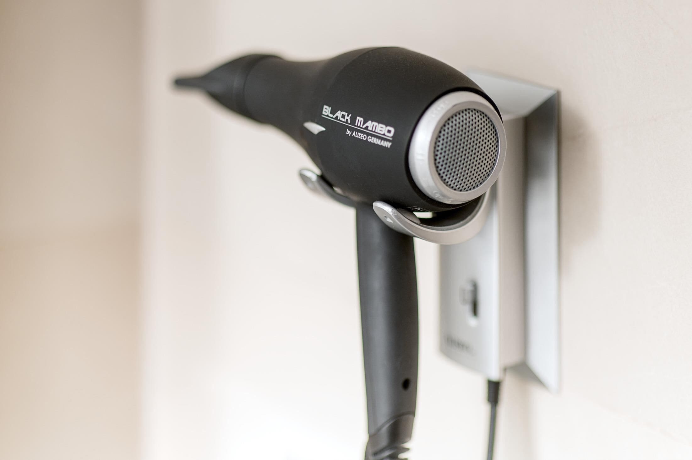 A black hairdryer mounted on a wall with a cord plugged in.