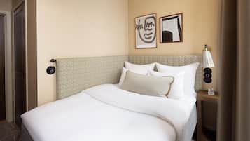 A hotel room with a large bed, a bedside table with a lamp, and two framed artworks on the wall.