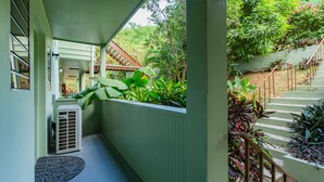 Un'area esterna riparata con una scala che conduce a un giardino, un piccolo condizionatore d'aria e una porta con un tappetino.