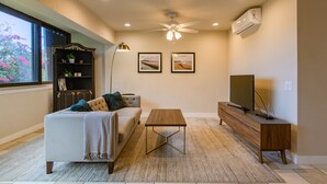 Un soggiorno con divano, tavolino, televisore, libreria e ventilatore a soffitto.