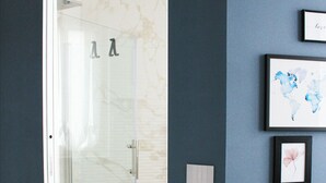 Une salle de bain moderne dotée d’une douche à parois de verre, d’un sol en marbre et d’un mur orné d’œuvres d’art encadrées.