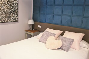 Cozy retreat with a heart-shaped pillow, bedside table, and wall art.