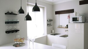 Une cuisine moderne avec des meubles blancs, des suspensions noires, une fenêtre et un four à micro-ondes posé sur le plan de travail.