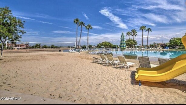 Une plage avec une piscine, des chaises longues et un toboggan jaune.