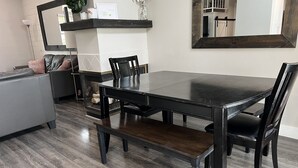 Un coin repas avec une table et des chaises en bois foncé, un banc et un mur blanc orné d’un grand miroir.