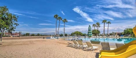 Une plage avec une piscine, des chaises longues et un toboggan jaune.