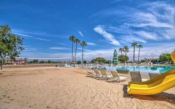 Una playa con piscina, sillas de descanso y un tobogán amarillo.