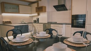 A modern kitchen with white cabinets, a built-in oven, and a dining table set with white plates, bowls, and wine glasses. - 164 apt. - Spacious & exclusive appartment with view (Pfitsch)