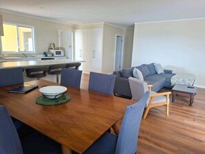 A modern living room with a wooden dining table, blue chairs, a grey sofa, and a small coffee table. - Holiday house for the whole family (Portland North)