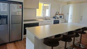 A modern kitchen with a central island, stainless steel appliances, and white cabinetry. - Holiday house for the whole family (Portland North)