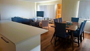 A modern living room with a dining area, a flat-screen TV, and a large window. - Holiday house for the whole family (Portland North)