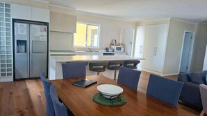 A modern kitchen with a central island, a dining table with chairs, and a sofa in the living area. - Holiday house for the whole family (Portland North)