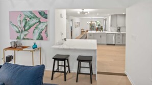 Ett modernt kök med vita skåp, en bänkskiva i marmor och en matplats med två barstolar.