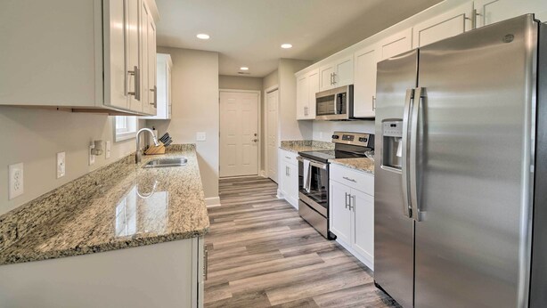 A modern kitchen with white cabinets, granite countertops, stainless steel appliances, and a wooden floor. - 3 Mi to Golf: Loris Home w/ Big Private Yard! (Loris)