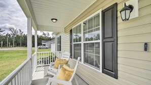 A covered porch with two white chairs and yellow cushions, a white railing, and a house with beige siding and black shutters. - 3 Mi to Golf: Loris Home w/ Big Private Yard! (Loris)