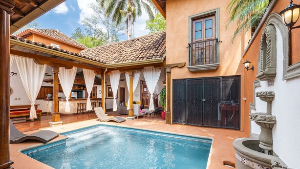 A swimming pool with a tiled deck, a covered seating area, and a stone fountain. - Casa Leon - colonial home with indoor pool (Tamarindo)
