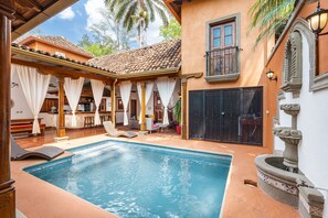 A swimming pool with a tiled deck, a covered seating area, and a stone fountain. - Casa Leon - colonial home with indoor pool (Tamarindo)
