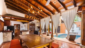 A spacious kitchen with wooden beams, a dining area with a large wooden table, and a pool area with a view of the outside. - Casa Leon - colonial home with indoor pool (Tamarindo)