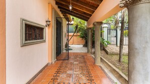 A covered outdoor corridor with tiled flooring, a wooden ceiling, and a metal gate leading to a garden area. - Casa Leon - colonial home with indoor pool (Tamarindo)
