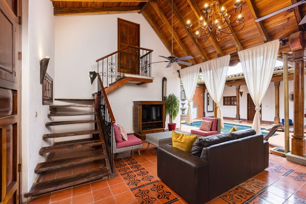 A spacious living area with a staircase, a sofa, a television, and a pool area. - Casa Leon - colonial home with indoor pool (Tamarindo)