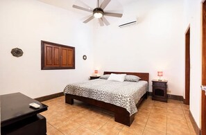 A bedroom with a bed, a desk, a ceiling fan, and a nightstand with a lamp. - Casa Leon - colonial home with indoor pool (Tamarindo)