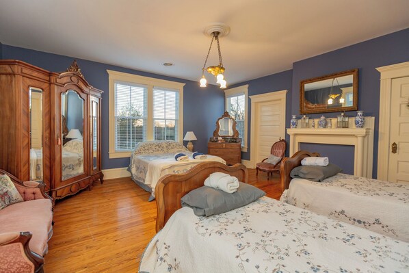 A bedroom with two beds, a wooden wardrobe, a mirror, and a fireplace.