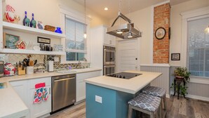 Een moderne keuken met witte kasten, een blauw eiland, roestvrijstalen apparatuur en een accentmuur van baksteen.