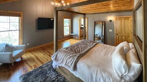 A bedroom with a wooden ceiling, a bed with white linens, a gray sofa, and a large window. - Secluded Sapphire Chalet w/ Game Room + Decks (Sapphire)