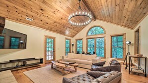 A spacious living room with a wooden ceiling, large windows, a sofa, a coffee table, and a television. - Secluded Sapphire Chalet w/ Game Room + Decks (Sapphire)