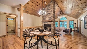 A spacious living area with a stone fireplace, wooden ceiling beams, and a dining table with chairs. - Secluded Sapphire Chalet w/ Game Room + Decks (Sapphire)
