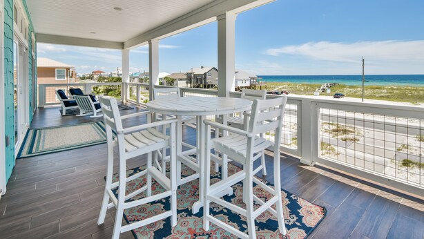 A covered outdoor area with a table and chairs, a view of the beach, and a railing. - Seas the Day-Gulf View Private Pool Home Across the Street from the Beach (Navarre)