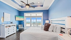 A bedroom with a large bed, a ceiling fan, a white dresser, a chair, and a view of the ocean through a large window. - Seas the Day-Gulf View Private Pool Home Across the Street from the Beach (Navarre)