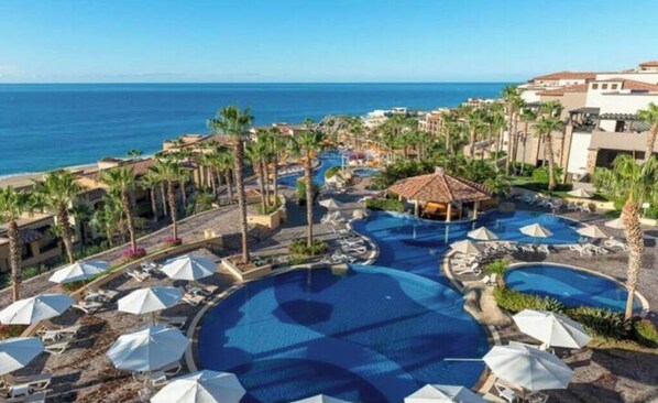 A resort with multiple swimming pools, palm trees, and a view of the ocean.