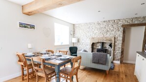 Ein Essbereich mit Holztisch und Stühlen, einer Steinwand mit Kamin und einer gemütlichen Sitzecke mit Sofa und Decke.