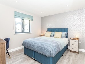 A bedroom with a bed, bedside tables, a window with curtains, and a view of buildings outside.