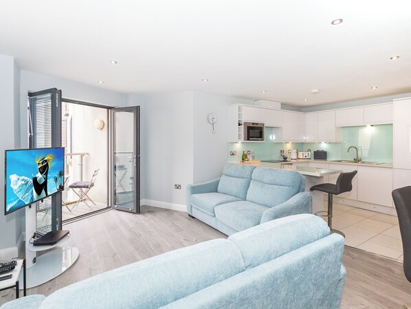 A modern living room with a light blue sofa, a flat-screen TV, and a glass door leading to a balcony.