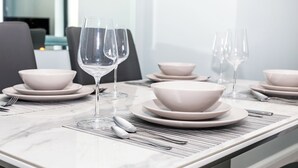A dining table set with white bowls, plates, and wine glasses, with a gray chair in the background. - 2 bedroom accommodation in Newquay (Newquay)