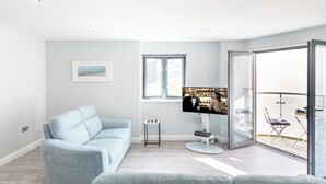 A modern living room with a light blue sofa, a flat-screen TV, and a large window. - 2 bedroom accommodation in Newquay (Newquay)