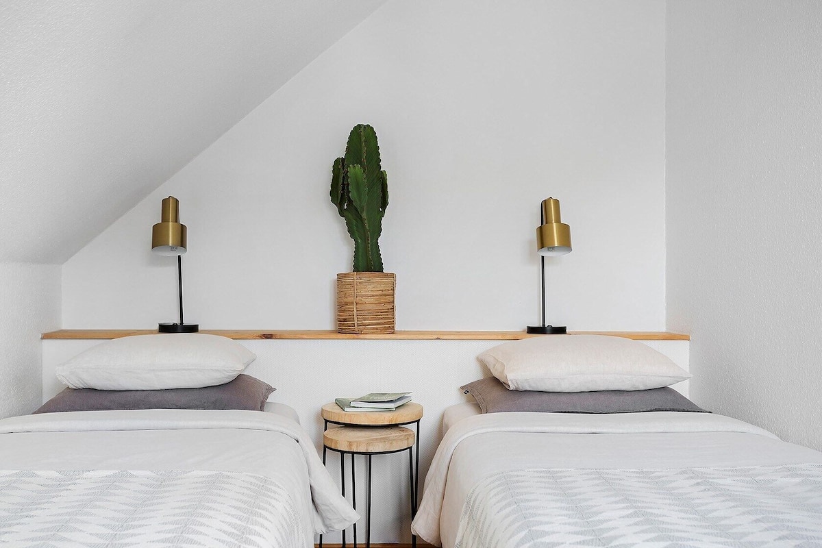 A bedroom with two beds, a wooden headboard, a small round table, two lamps, and a cactus plant.