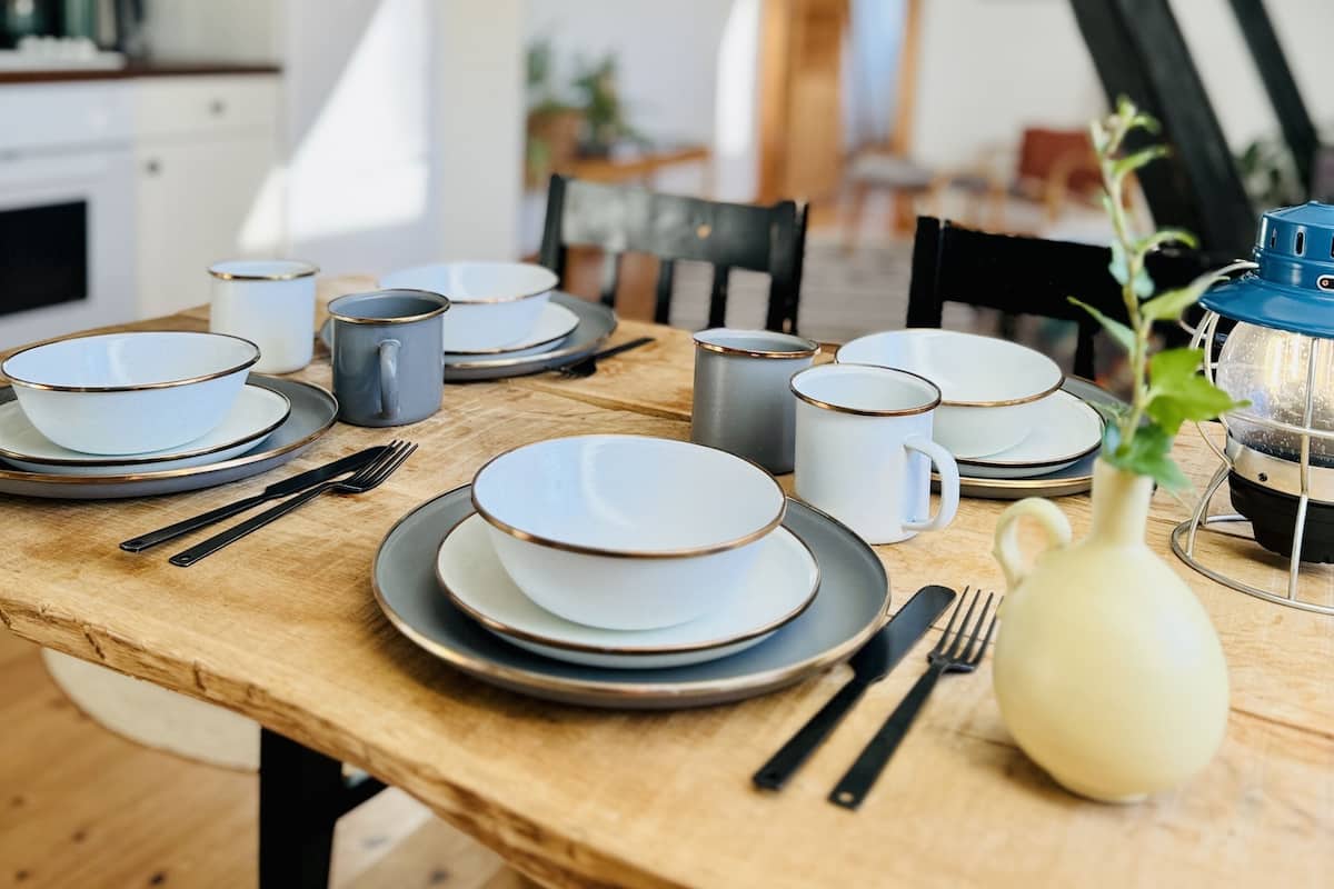 A dining table set with plates, bowls, and cups, with a vase of flowers and a lantern on the table.